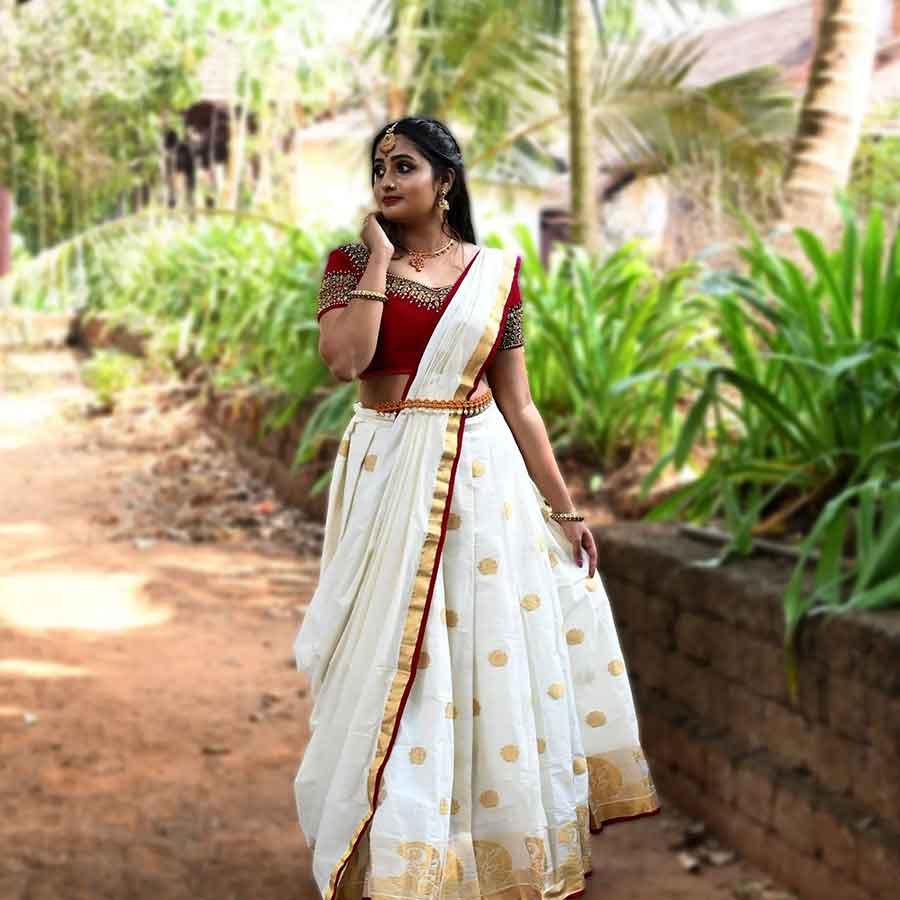 Setting the bridal trousseau trends high with our signature Kasavu Lehenga. A gorgeous ethnic attire, the maroon bodice is ornated with handcrafted zari and iconic motifs in decadent zardosi The voluminous skirt is crafted in Kerala Kasavu with Jacquard borders. Complementing the attire, is a pristine dupatta with zari buttas and contrast edging.